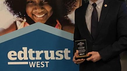 Asm. Muratsuchi holding award and standing next to EdTrust-West banner