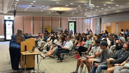 Guest speaker at podium, speaking to large seated audience