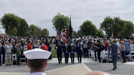 Armed service members carrying flags, with large audience on either side