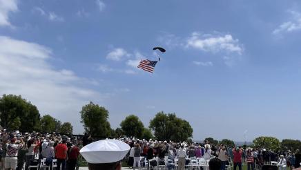 Audience watches military member parachuting down with large American flag