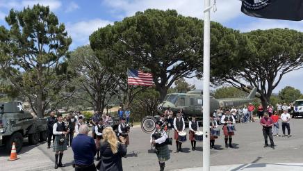 Bagpipe band in Scottish garb playing between armored vehicle and helicopter