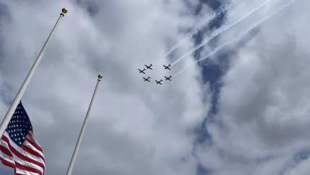 US and CA flags with military planes flying below clouds overhead