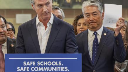 Gov. Newsom at podium with Asm. Muratsuchi, holding up signed document